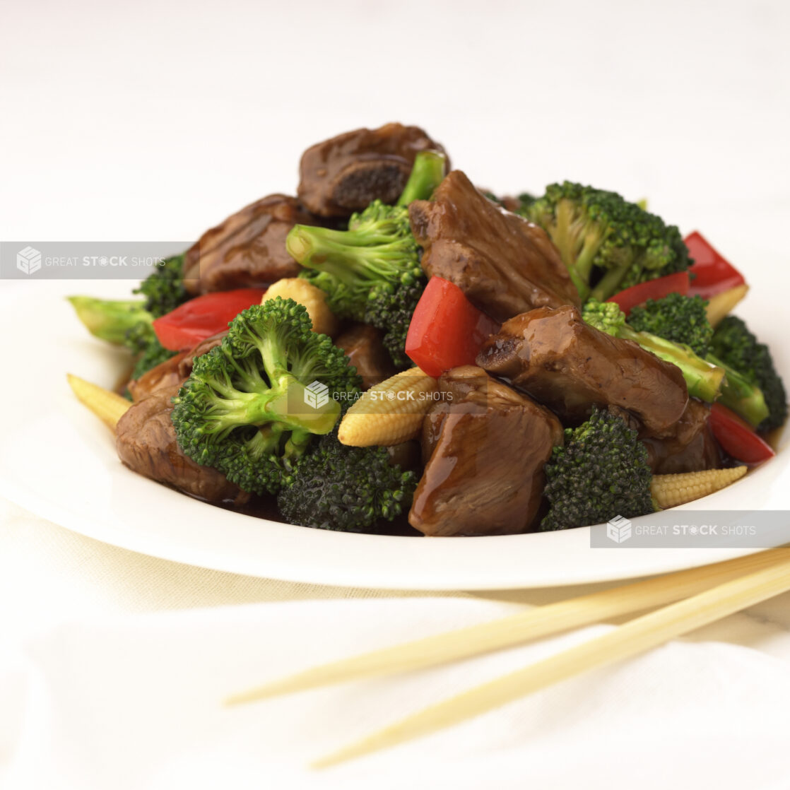 Close Up of a Dish of Beef and Vegetable Stir Fry with Baby Corn, Broccoli and Red Peppers on a White Ceramic Platter