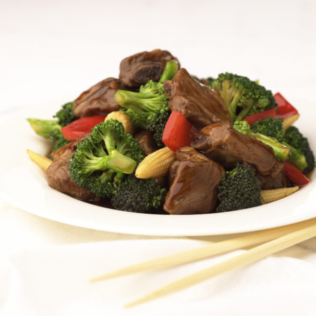 Close Up of a Dish of Beef and Vegetable Stir Fry with Baby Corn, Broccoli and Red Peppers on a White Ceramic Platter