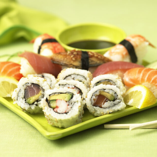 Assorted Maki Roll and Nigiri Sushi on a Green Plate on a Green Table Cloth Surface in an Indoor Setting