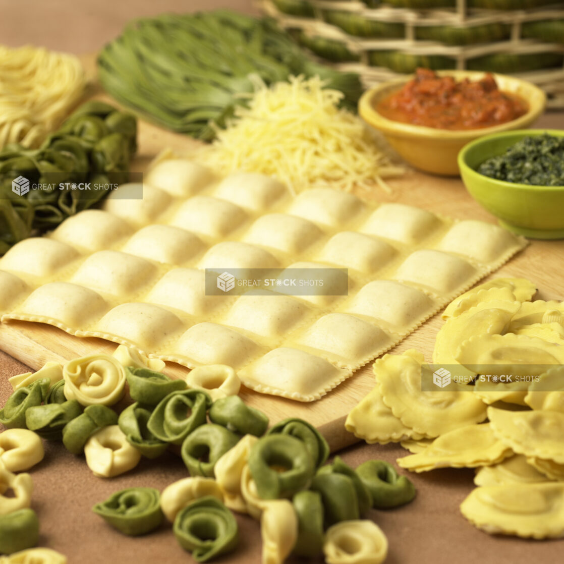 Assorted Fresh Pastas – Ravioli, Spinach Tortellini, Mezzalune and Linguine – on a Wooden Cutting Board in a Kitchen Setting