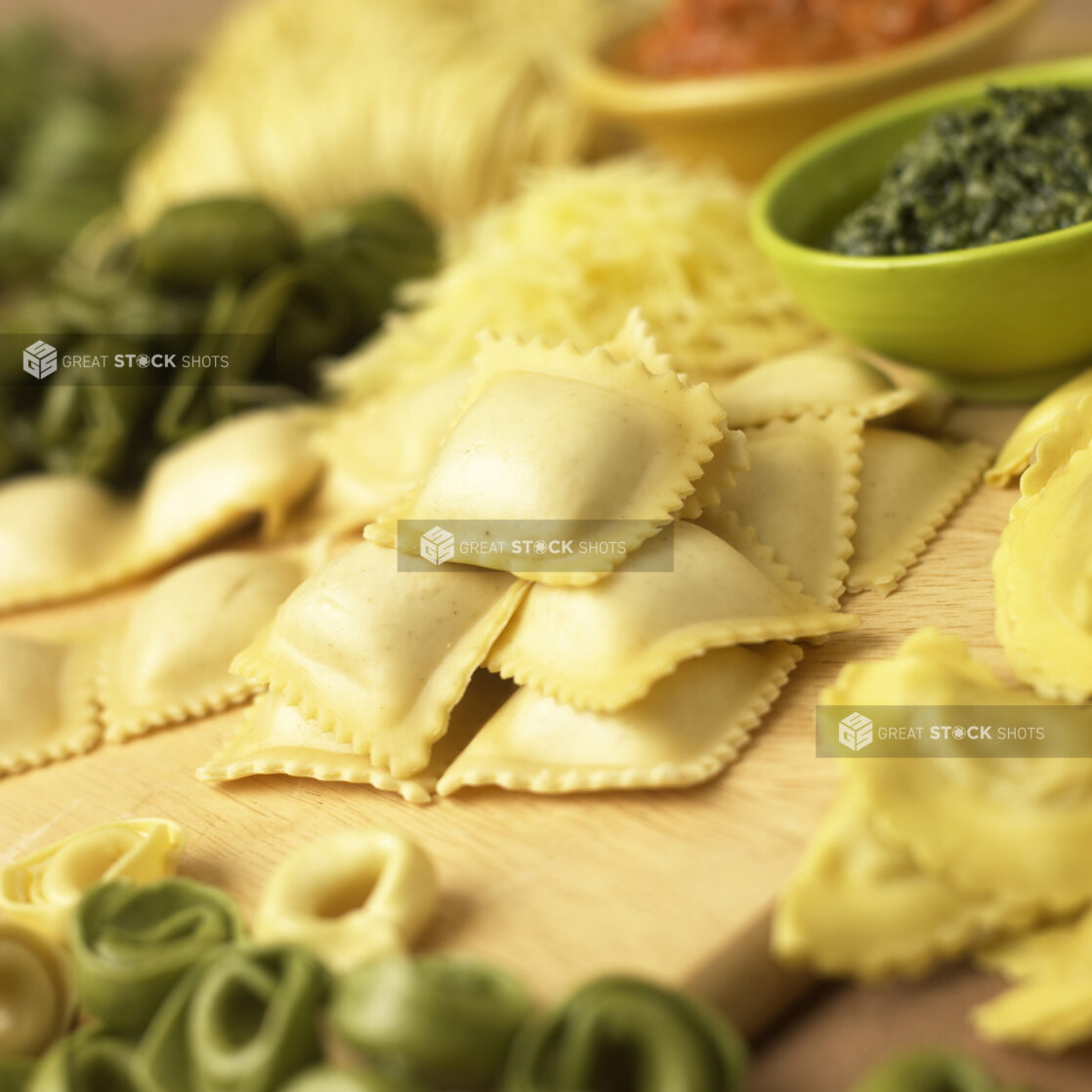 Close Up of Assorted Fresh Stuffed Pastas - Ravioli, Spinach Tortellini, Mezzalune - on a Wooden Cutting Board in a Kitchen Setting