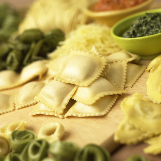 Close Up of Assorted Fresh Stuffed Pastas - Ravioli, Spinach Tortellini, Mezzalune - on a Wooden Cutting Board in a Kitchen Setting