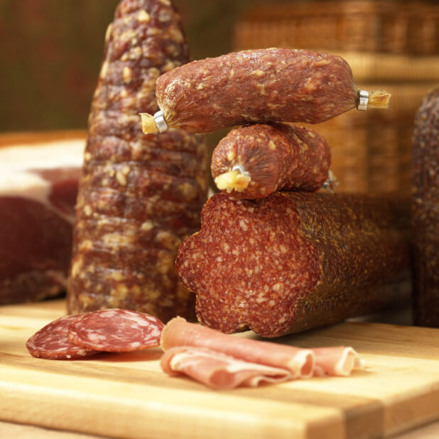 An Array of Whole and Sliced Cured Deli Meats on a Wooden Table in an Indoor Setting - Variation
