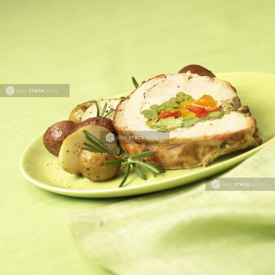 Dinner Combo Plate of Rolled Stuffed Chicken and Herb Roasted Potatoes on a Green Ceramic Plate on a Green Table Cloth Surface