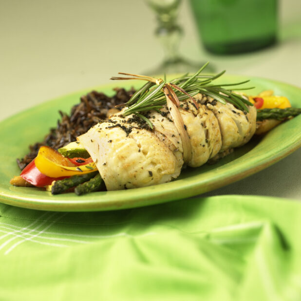 Rolled Sole Fillet Stuffed with Roasted Vegetables and a Side of Wild Rice on a Green Ceramic Dish on a Green Table Cloth Surface