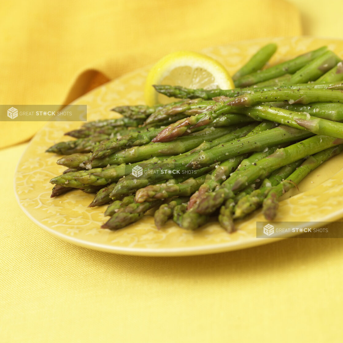 Close Up of Steamed Asparagus Spears on a Yellow Ceramic Dish on a Yellow Table Cloth Surface in an Indoor Setting