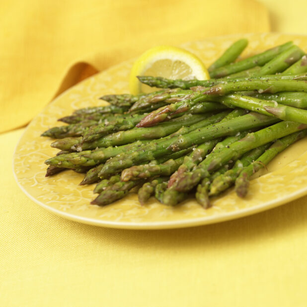 Close Up of Steamed Asparagus Spears on a Yellow Ceramic Dish on a Yellow Table Cloth Surface in an Indoor Setting