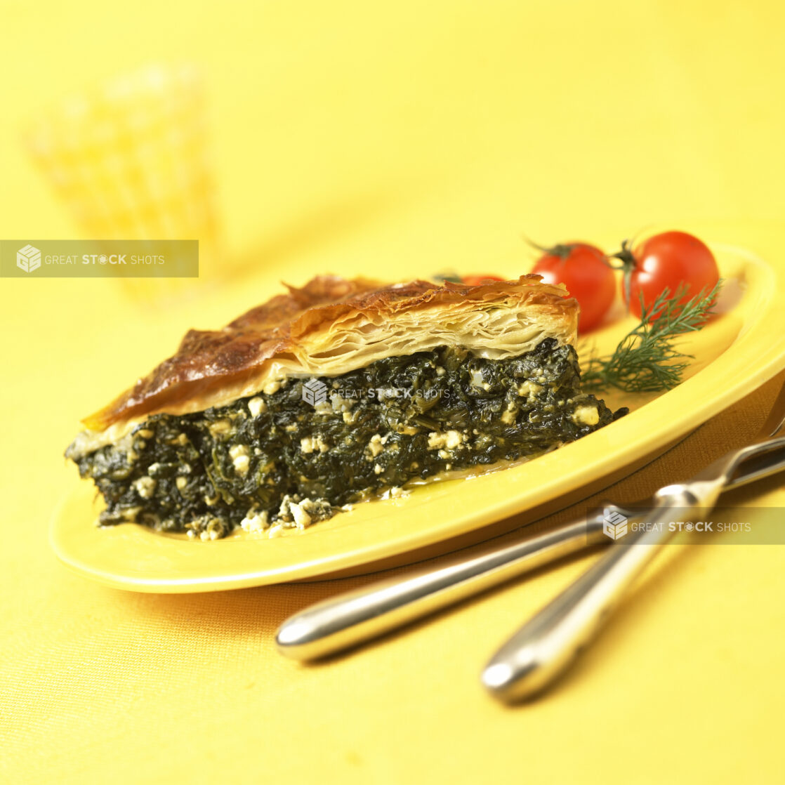 A Slice of Spanakopita - Greek Spinach Pie - on a Yellow Ceramic Dish on a Yellow Table Cloth Surface