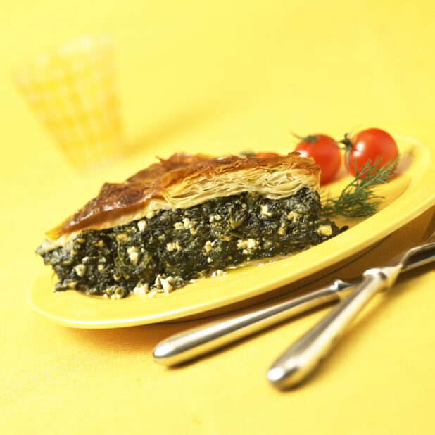A Slice of Spanakopita - Greek Spinach Pie - on a Yellow Ceramic Dish on a Yellow Table Cloth Surface