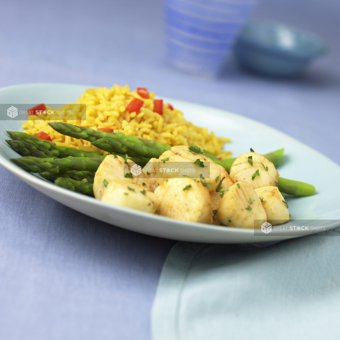 Seafood Dinner Combo with Sautéed Scallops, Steamed Asparagus and Rice Pilaf in a Blue Ceramic Dish on a Blue Table Cloth Surface