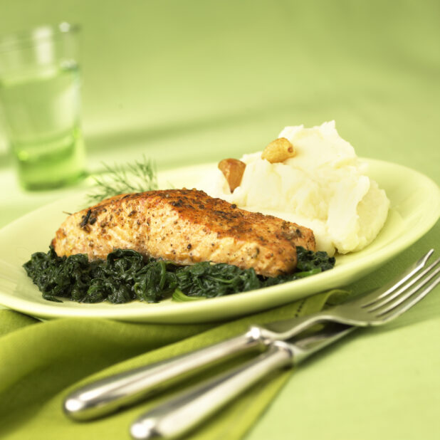 Dinner Combo Plate with Grilled Herb Crusted Salmon on a Bed of Sautéed Spinach with a Side of Garlic Mashed Potatoes in a Green Ceramic Dish on a Green Table Cloth Surface