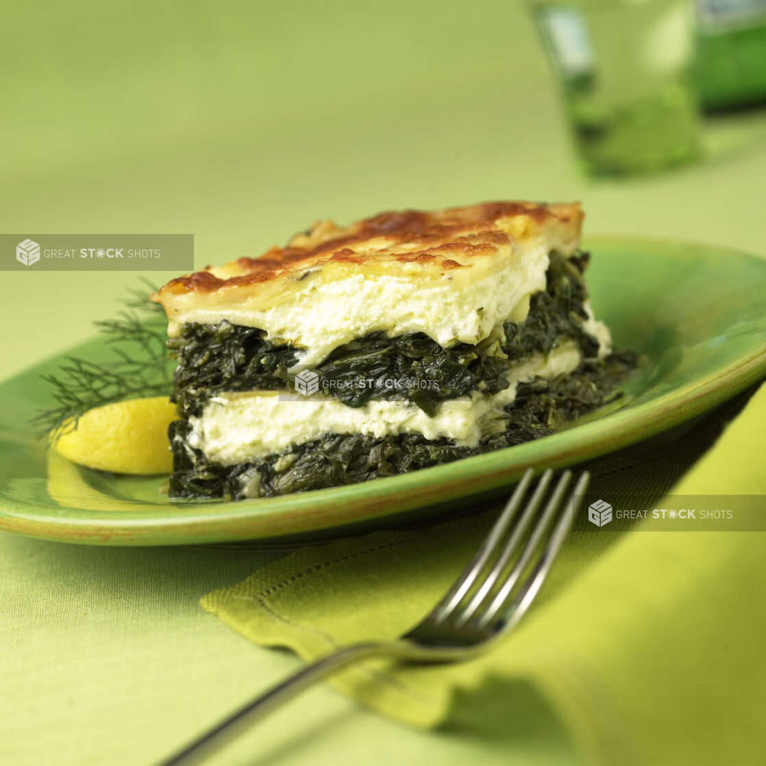 A Block of Greek Spanakopita - Spinach and Cheese Pie - on a Green Ceramic Dish on a Green Table Cloth Surface