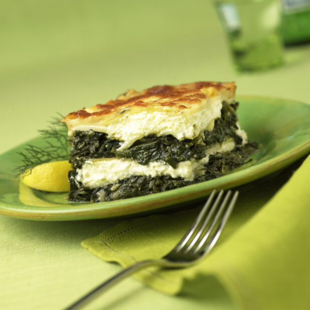 A Block of Greek Spanakopita - Spinach and Cheese Pie - on a Green Ceramic Dish on a Green Table Cloth Surface
