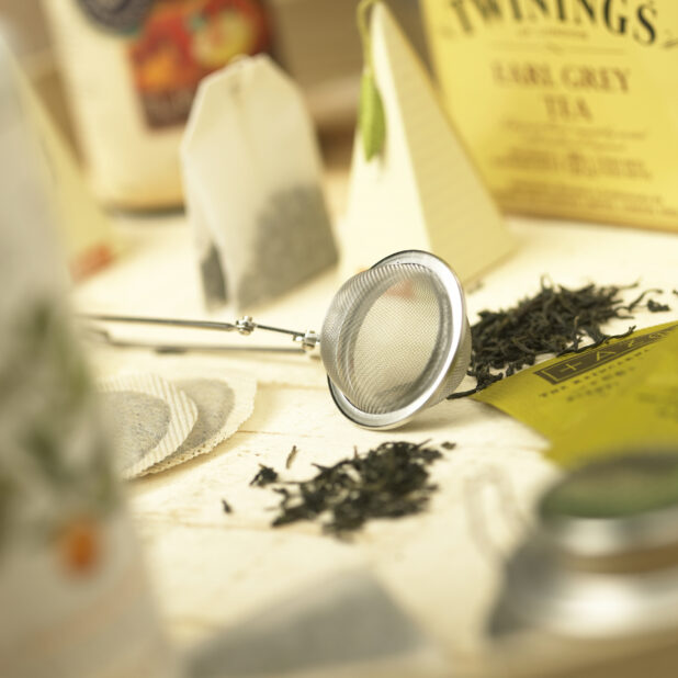 Close Up of a Tea Strainer and Loose Leaf and Bagged Tea in an Indoor Setting