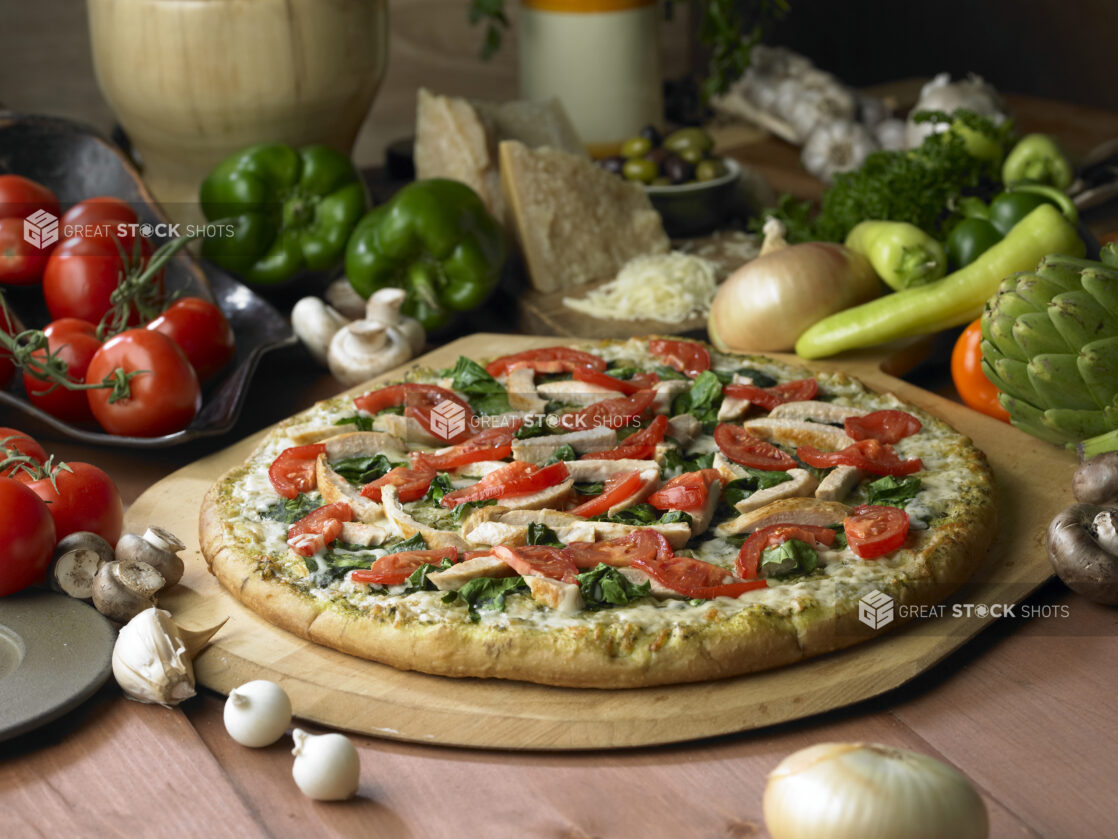 Whole Pizza with Spinach, Tomatoes, Chicken Strips and Pesto Sauce on a Wooden Pizza Peel on a Wooden Table