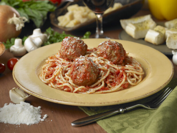 Spaghetti and Meatballs in a Yellow Ceramic Dish on a Wooden Table in an Indoor Setting