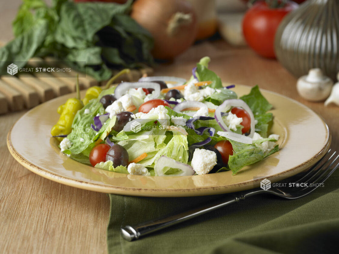 Greek Salad with Cherry Tomatoes, Kalamata Olives and Pepperoncini Peppers on a Yellow Ceramic Dish on a Wooden Table