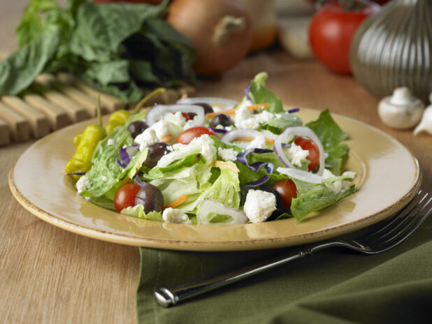 Greek Salad with Cherry Tomatoes, Kalamata Olives and Pepperoncini Peppers on a Yellow Ceramic Dish on a Wooden Table