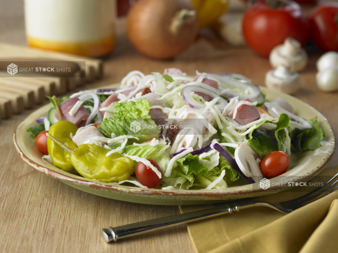 Chef Salad with Grape Tomatoes, Rolled Deli Meats, Shredded Cheese and Pepperoncini Peppers in a Yellow Ceramic Dish on a Wooden Table