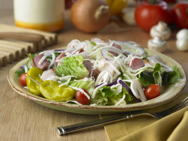 Chef Salad with Grape Tomatoes, Rolled Deli Meats, Shredded Cheese and Pepperoncini Peppers in a Yellow Ceramic Dish on a Wooden Table