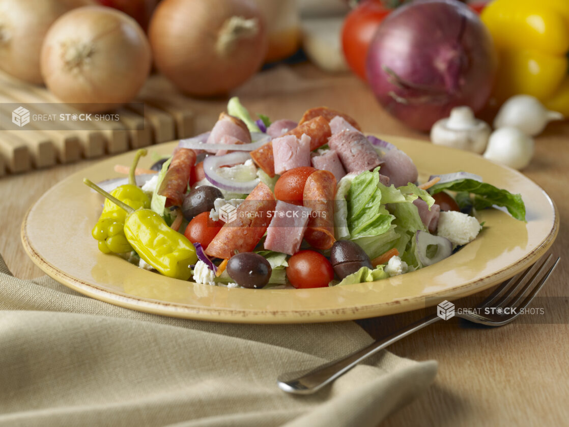 Antipasto Salad with Cherry Tomatoes, Italian Deli Meats, Kalamata Olives and Pepperoncini Peppers in a Yellow Ceramic Dish on a Wooden Table