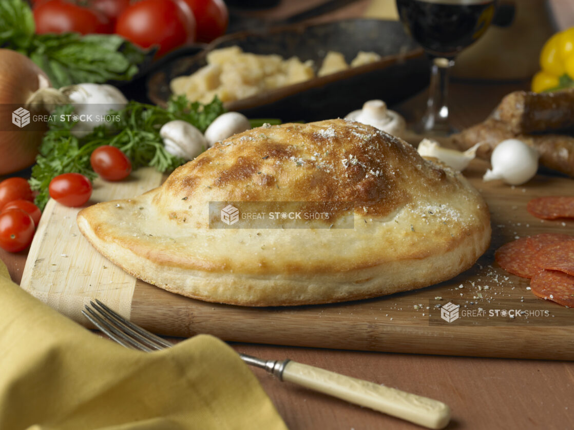 A Whole, Uncut Calzone on a Wooden Cutting Board in an Kitchen Setting