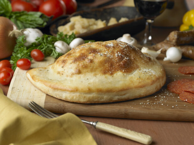 A Whole, Uncut Calzone on a Wooden Cutting Board in an Kitchen Setting