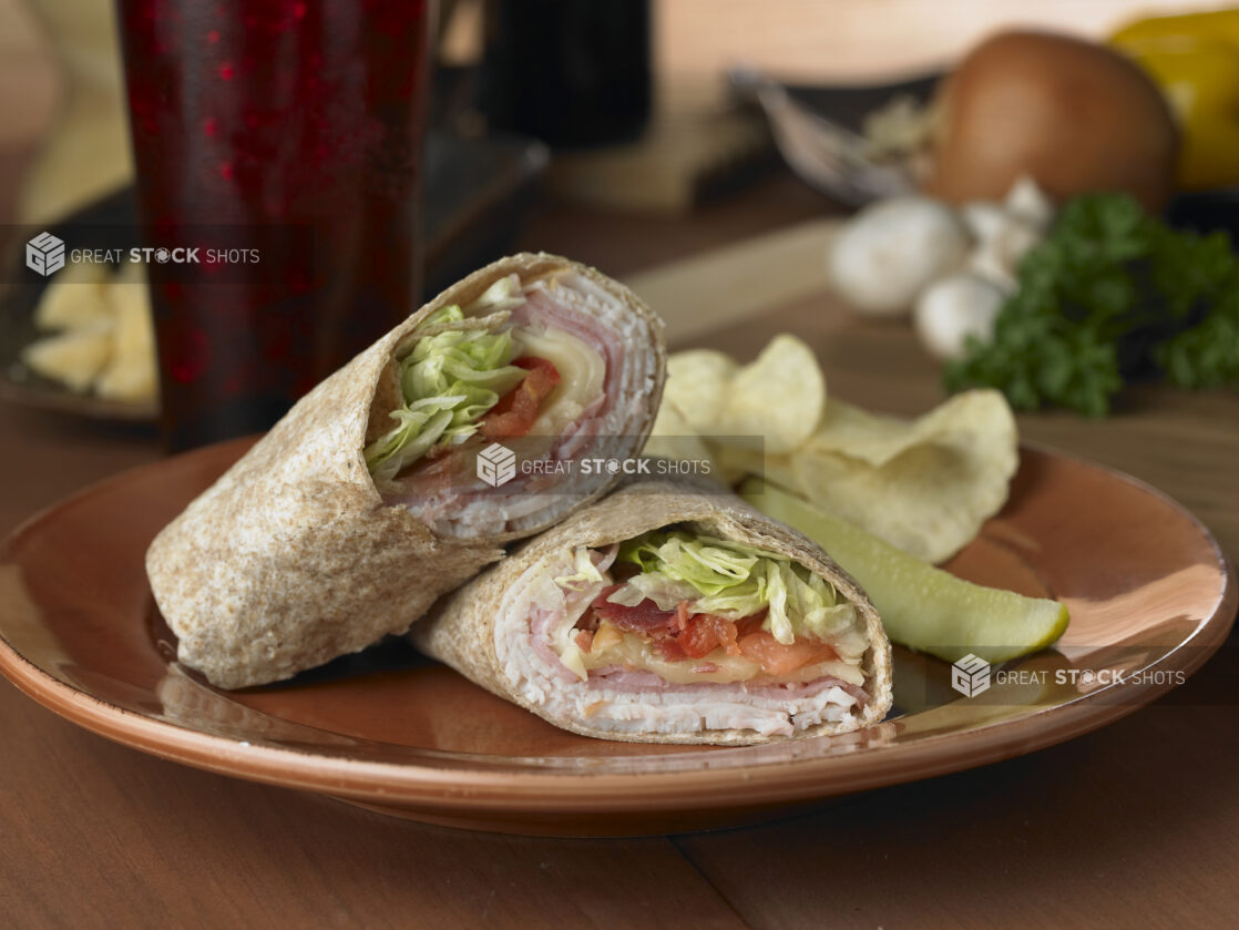 Turkey, Ham and Swiss in a Whole Wheat Wrap with Fresh Vegetables and a Pickle Spear on a Brown Ceramic Dish on a Wooden Table