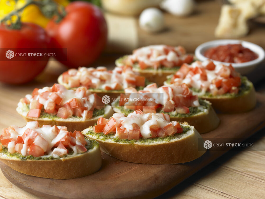 Tomato Pesto Bruschetta on Sliced Italian Bread on a Wooden Cutting Board in a Kitchen Setting