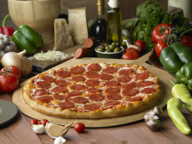 A Whole Pepperoni Pizza on a Wooden Pizza Peel on a Wooden Table in a Kitchen Setting