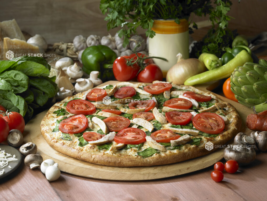 Whole Pizza with Spinach, Tomatoes, Chicken Strips and Pesto Sauce on a Wooden Pizza Peel on a Wooden Table - Variation