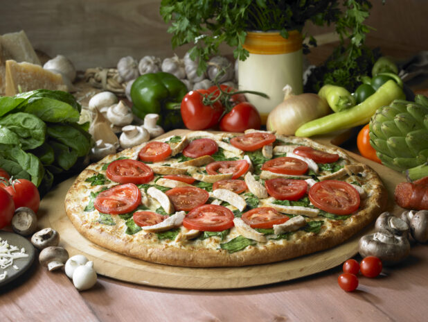 Whole Pizza with Spinach, Tomatoes, Chicken Strips and Pesto Sauce on a Wooden Pizza Peel on a Wooden Table - Variation