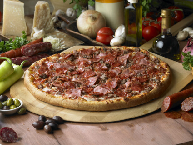 Whole Meat Lovers Pizza with Sliced Ham, Pepperoni, Bacon and Ground Beef on a Wooden Pizza Peel in a Indoor Setting