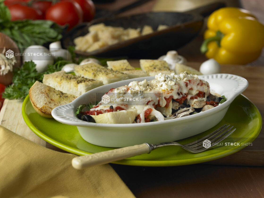 Vegetable Pasta Bake in an Individual Casserole Dish with a Side of Garlic Bread Slices on a Green Ceramic Dish in an Indoor Setting