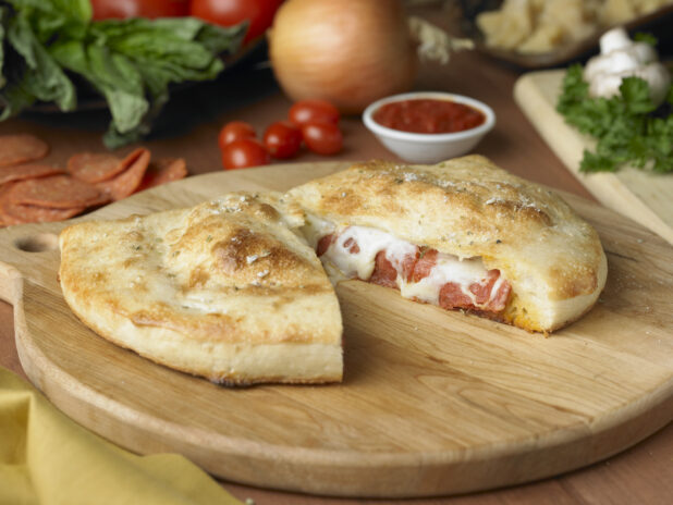 A Pepperoni and Cheese Calzone Cut in Half on a Wooden Cutting Board in a Kitchen Setting