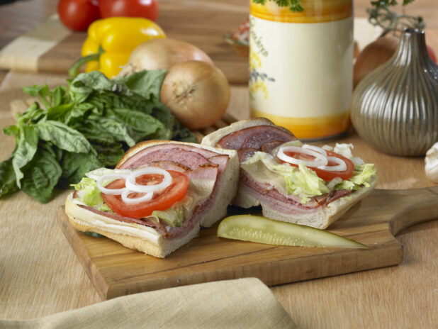An Open-Faced Italian Sub Sandwich Cut in Half on a Wooden Cutting Board with a Pickle Spear in a Kitchen Setting