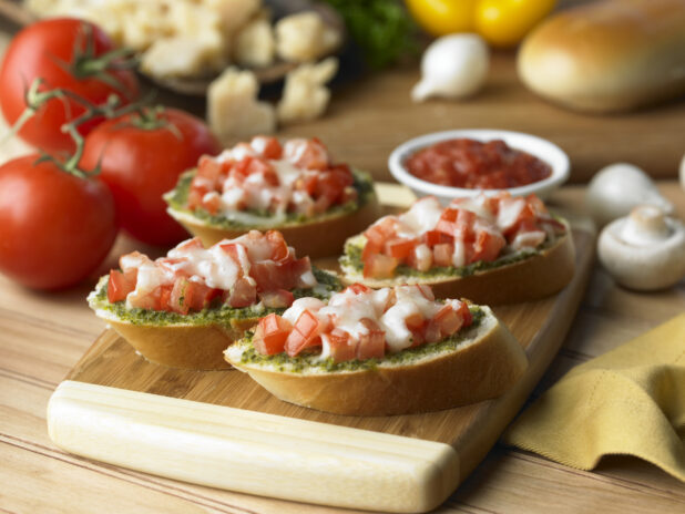 Tomato Pesto Bruschetta on Sliced Italian Bread on a Wooden Cutting Board in a Kitchen Setting - Variation