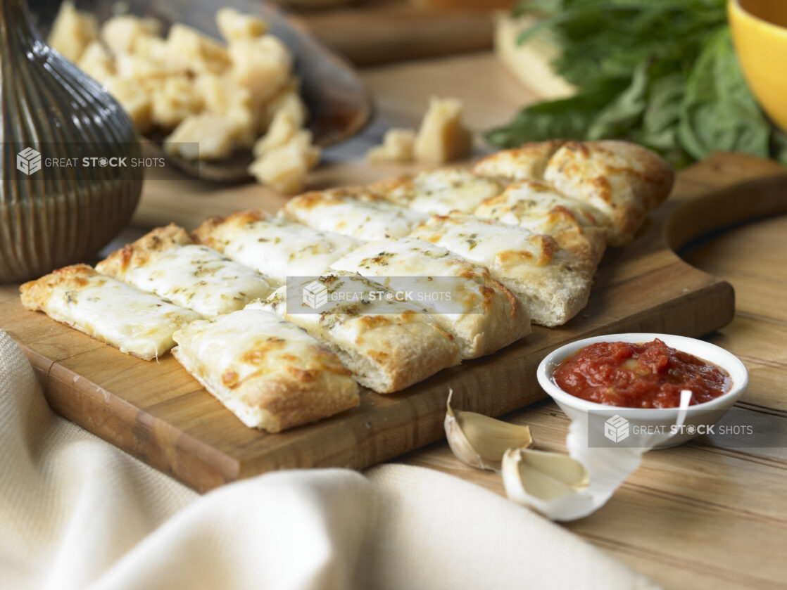 Cheesy Garlic Fingers with a Side of Marinara Sauce on a Wooden Cutting Board in a Kitchen Setting