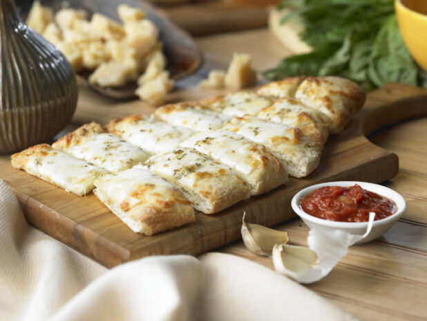 Cheesy Garlic Fingers with a Side of Marinara Sauce on a Wooden Cutting Board in a Kitchen Setting