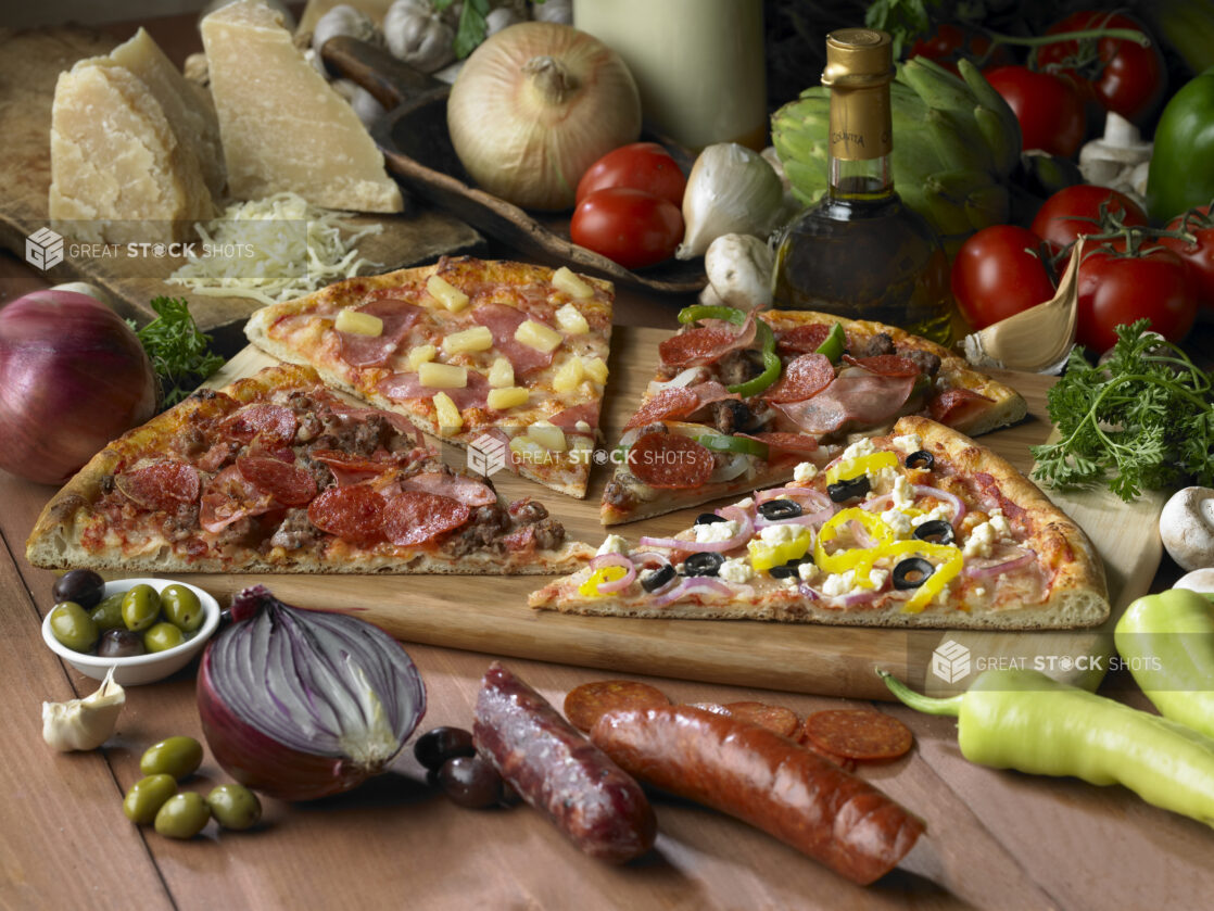 Assorted Specialty Pizza Slices - Meat Lovers, Hawaiian, Deluxe, Greek - on a Wooden Cutting Board on a Wooden Table