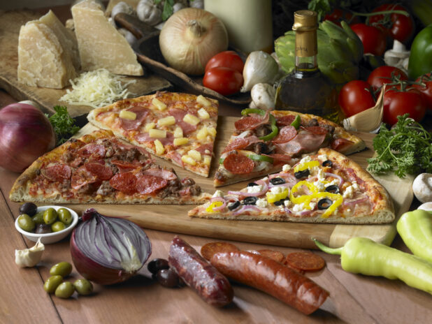 Assorted Specialty Pizza Slices - Meat Lovers, Hawaiian, Deluxe, Greek - on a Wooden Cutting Board on a Wooden Table