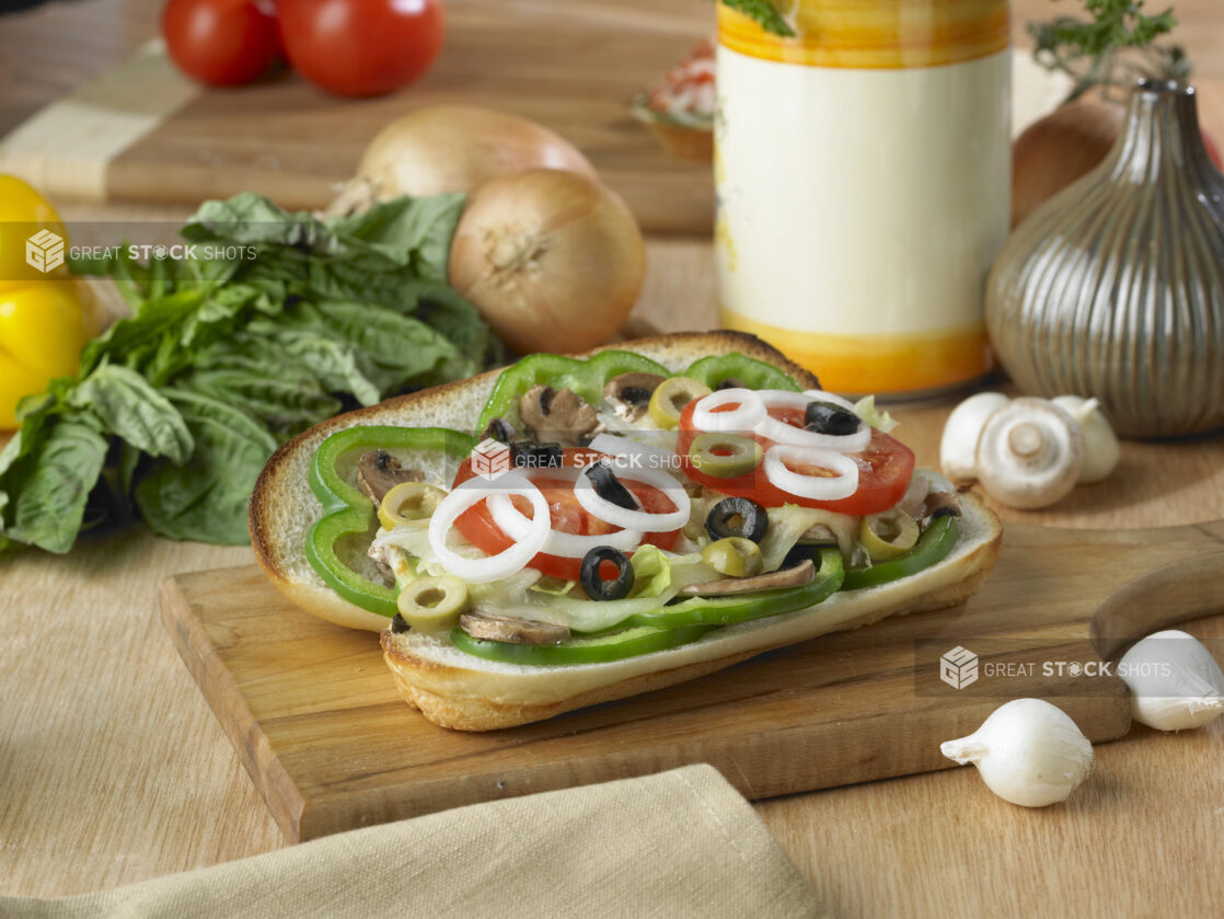 Open-Faced Vegetarian Sub Sandwich with Sautéed Mushrooms, Green and Black Olives on a Wooden Cutting Board in an Indoor Setting