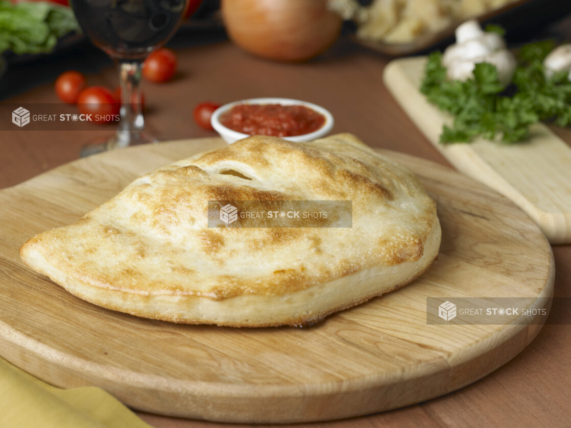 A Whole, Uncut Calzone on a Wooden Cutting Board in an Kitchen Setting - Variation