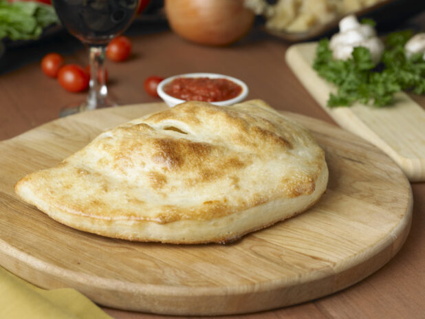 A Whole, Uncut Calzone on a Wooden Cutting Board in an Kitchen Setting - Variation