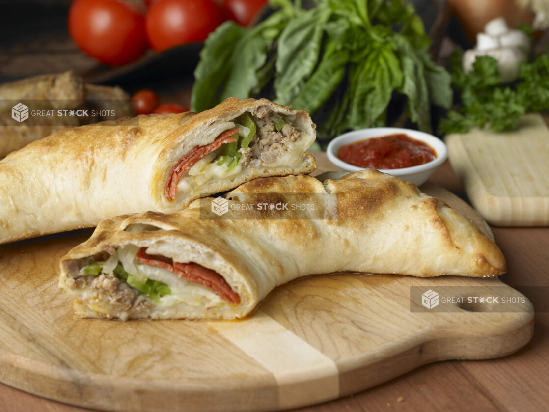 A Deluxe Stromboli Cut in Half on a Wooden Cutting Board with a Side of Marinara Sauce in a Kitchen Setting