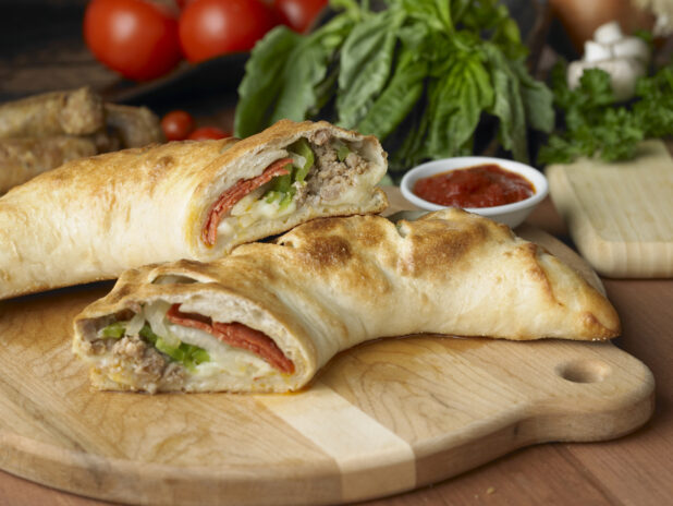 A Deluxe Stromboli Cut in Half on a Wooden Cutting Board with a Side of Marinara Sauce in a Kitchen Setting
