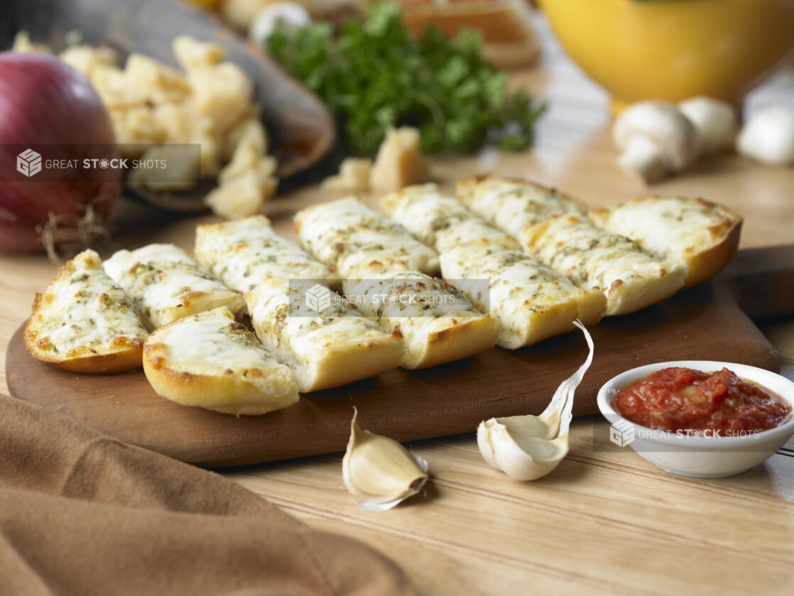 Cheesy Garlic Bread on Toasted, Sliced Sub Roll Bread with a Side of Marinara Sauce on a Wooden Cutting Board in a Kitchen Setting