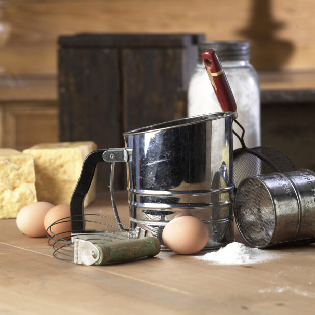 Flour Sifter, Pastry Blender and Eggs on a Wooden Table in a Kitchen Setting