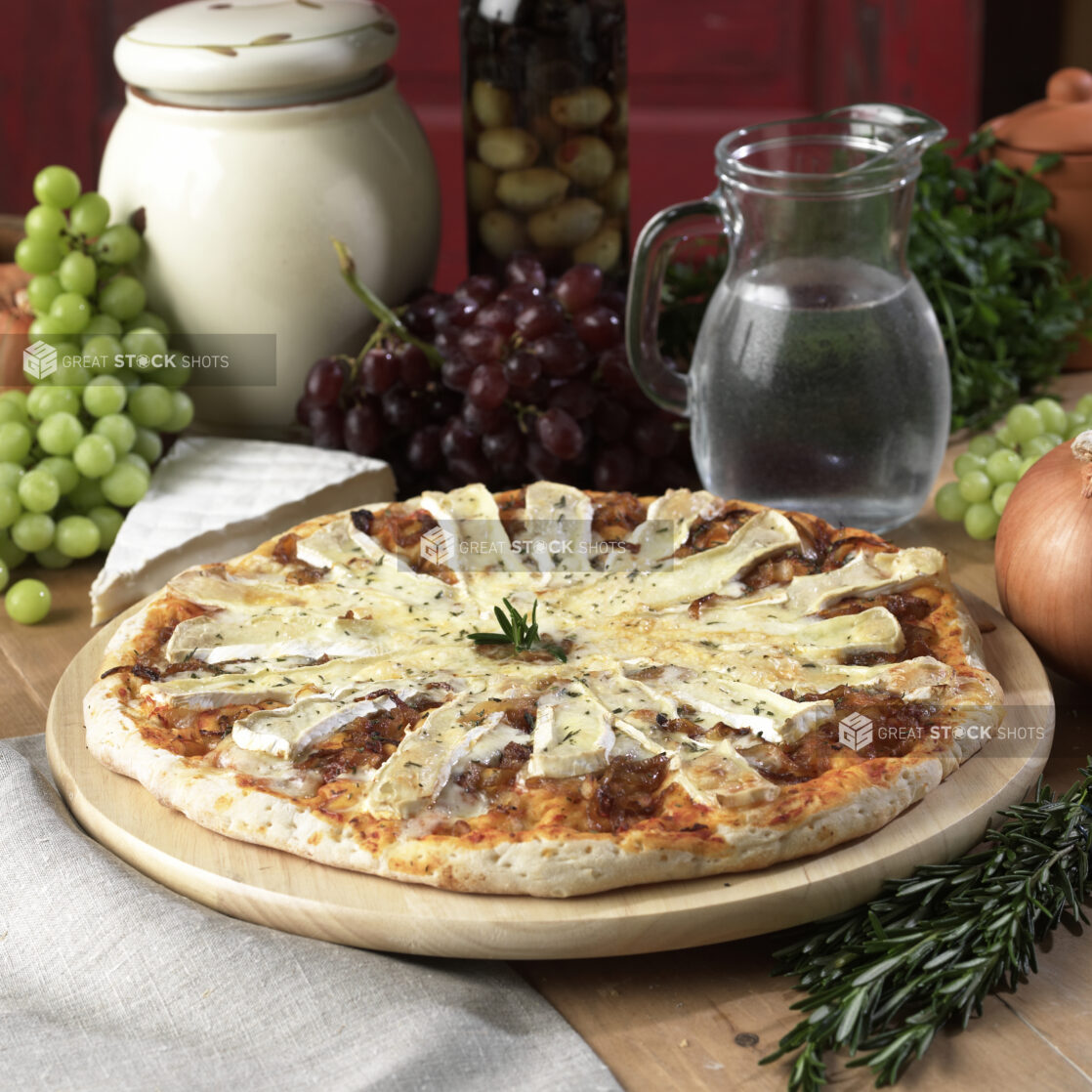 Whole Pizza with Brie Cheese Slices and Caramelized Onion Toppings on a Wooden Pizza Platter on a Wooden Table in an Indoor Setting