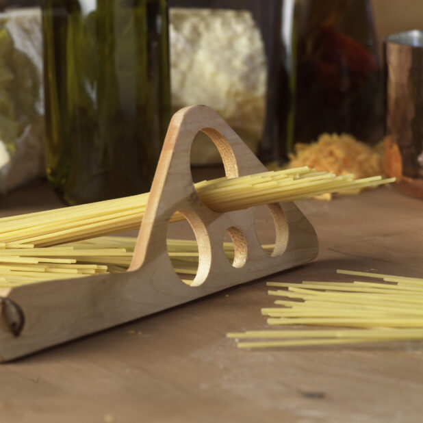 Dry Spaghetti Noodles in a Wooden Pasta Portion Measuring Tool on a Wooden Cutting Board in a Kitchen Setting